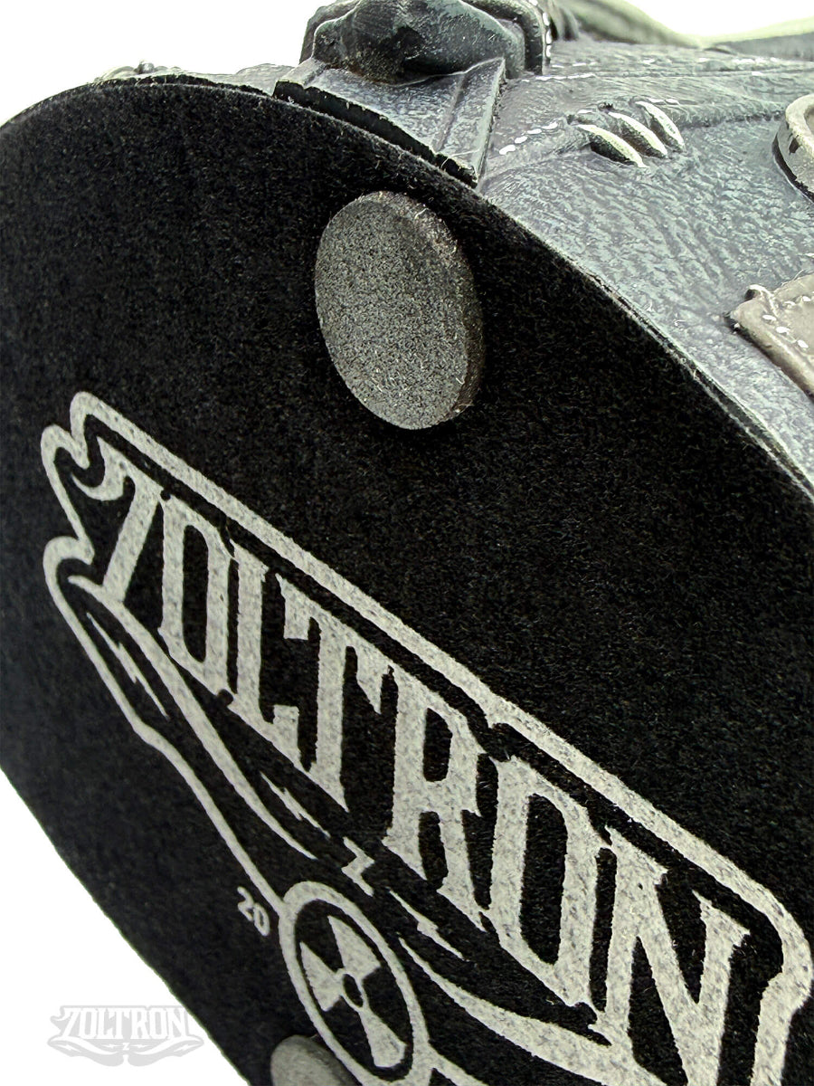 A  close-up of a the bottom silkscreened, felt base of a highly detailed resin and soapstone sculpture by artist Zoltron, featuring a highly detailed skull figurine wearing a cracked leather aviator helmet, a weathered black leather jacket, war medallions and adornments, smoking a cigarette, set against a plain white background.