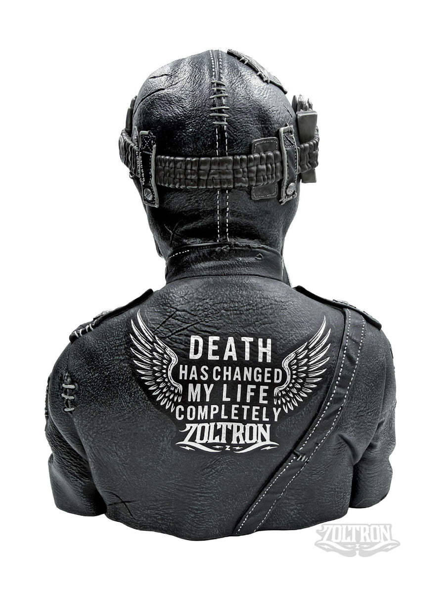 A backview close-up of a highly detailed resin and soapstone sculpture by artist Zoltron, featuring a highly detailed skull figurine wearing a cracked leather aviator helmet, a weathered black leather jacket adorned with the phrase DEATH HAS CHANGED MY LIFE COMPLETELY. war medallions and adornments, stitching and distress from time,  set against a plain white background.